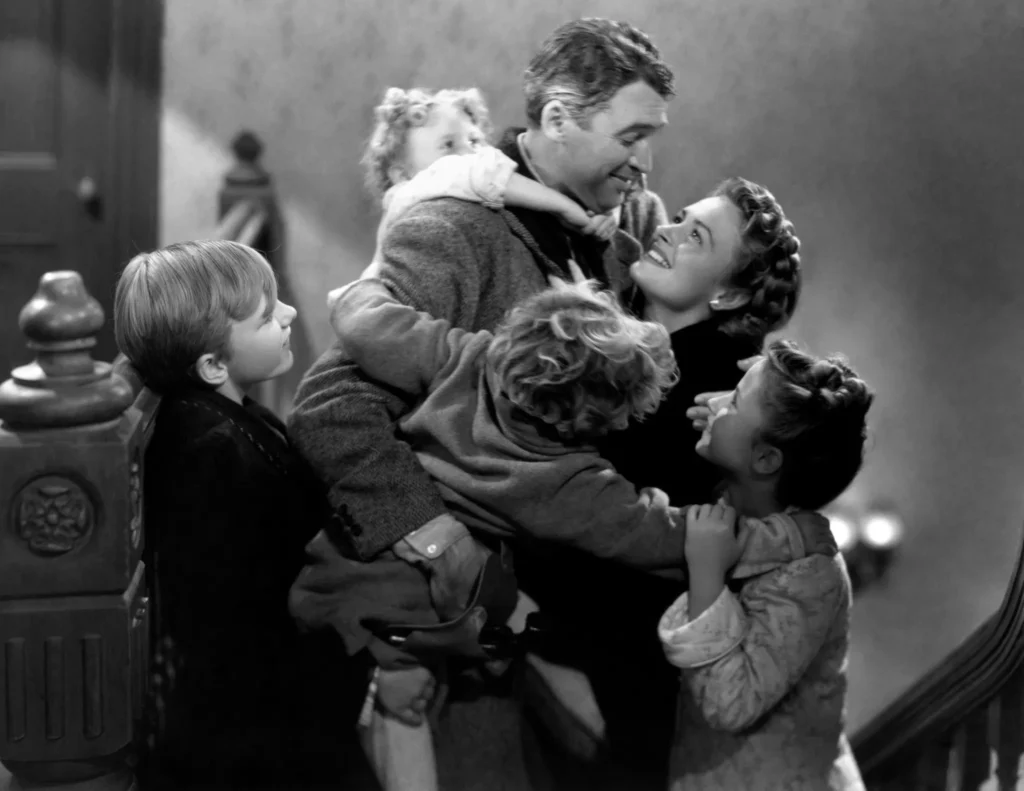 A joyful black-and-white scene of a family hugging a man near a staircase. The mood is celebratory and loving.